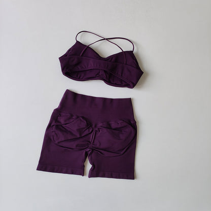 A two-piece swimwear set in deep purple, featuring a strappy bandeau-style bikini top and matching high-waisted shorts with a gathered front detail, laid flat on a light gray background.