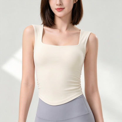 A woman wearing a fitted sleeveless top with a square neckline and gathered side detail, shown from the shoulders to the hips against a light neutral studio background.